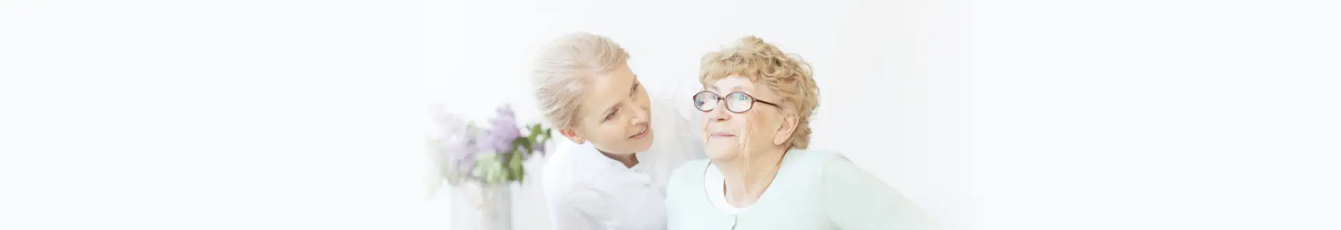 Young caregiver assisting smiling elderly lady in standing up from chair.