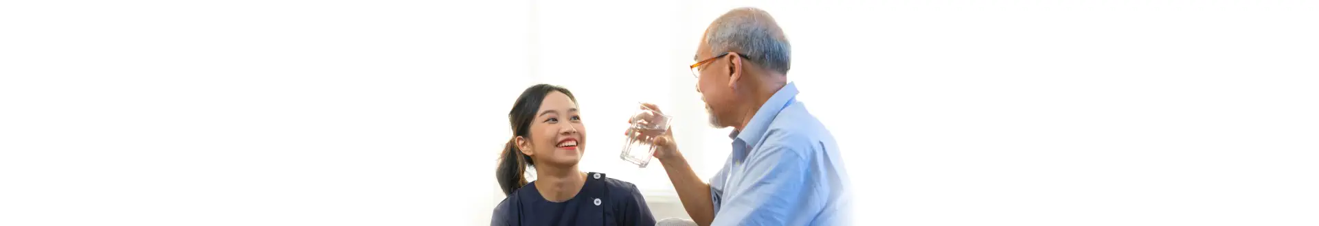 Smiling nurse giving glass of water to elderly patient in nursing home